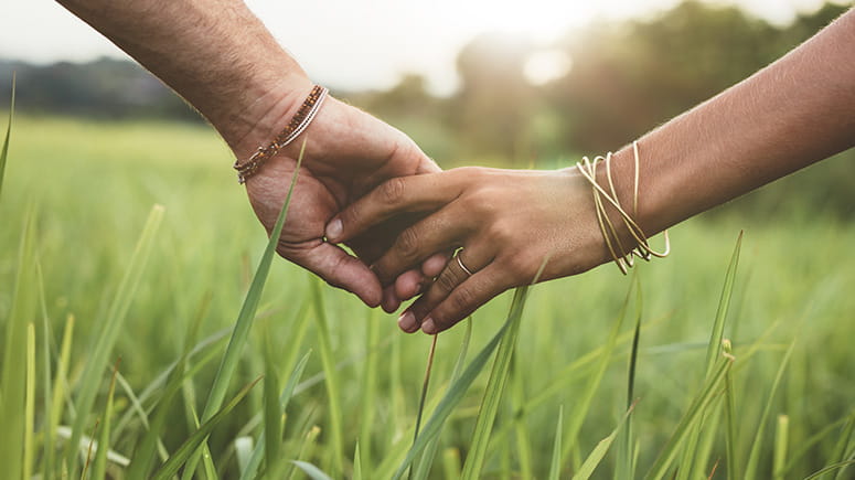 A man and a woman holding hands in a grassy field.